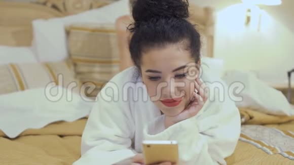 漂亮的红唇黑发女人在酒店房间的床上躺着电话视频的预览图