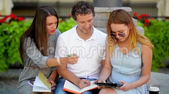 一群带笔记的学生坐在户外的长凳上用黑色平板电脑为考试做准备视频的预览图