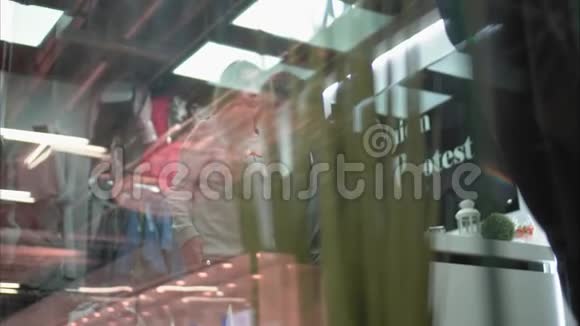 女孩在商店里试穿一件新的时尚运动衫购物透过窗户观看视频的预览图