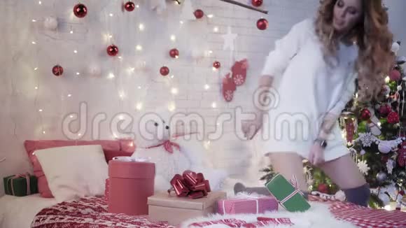 年轻的美女坐在圣诞树附近的床上包上新年礼物视频的预览图