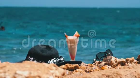 埃及海滩上的热带鲜榨果汁帽子和眼镜架在红海边的岩石上视频的预览图