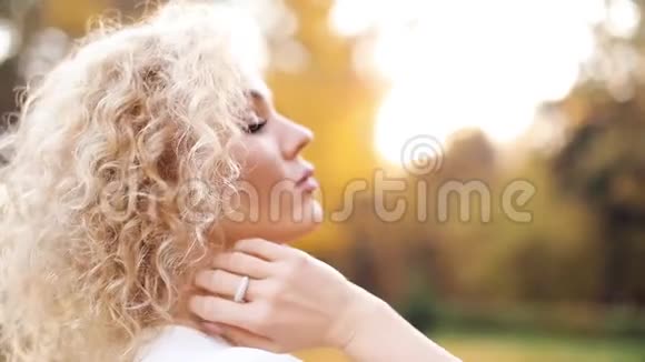 美丽的金发女人摸着卷发走在秋天的公园里视频的预览图