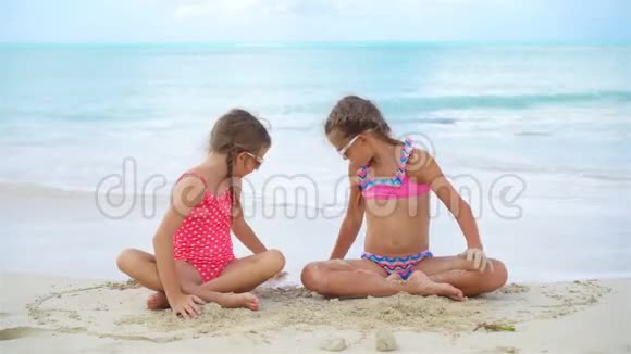 可爱的小女孩在海滩上玩沙子孩子们坐在浅水里做沙堡视频的预览图