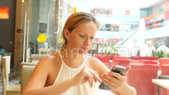 一个金发女人正坐在一个炎热的夏天的咖啡馆里微笑着在手机上输入短信4k慢视频的预览图