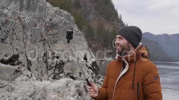 大胡子的游客正在与朋友在一条山河畔的手机上举行视频会议慢动作视频的预览图