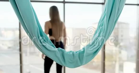 漂亮的年轻女人在有大窗户的房间里做飞行瑜伽运动有魅力的女性在她的身体里工作视频的预览图