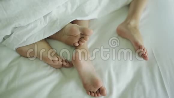 幸福家庭的两双腿躺在被子下的床上母亲和婴儿视频的预览图
