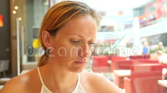 一个金发女人正坐在一个炎热的夏天的咖啡馆里微笑着在手机上输入短信4k慢视频的预览图