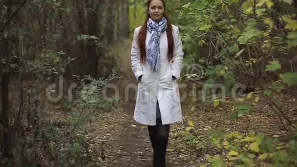 金发白种人中年妇女穿着白大褂在秋天公园的阴天散步视频的预览图