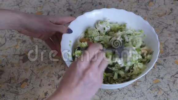 无法辨认的女人把蔬菜沙拉混合在厨房桌子上的一个白色盘子里把手举起来视频的预览图