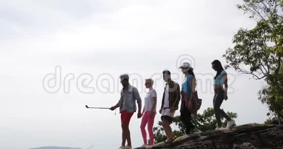 成群结队的游客在山顶上漫步手握镜头欢乐男女在美丽的风景天际线上视频的预览图