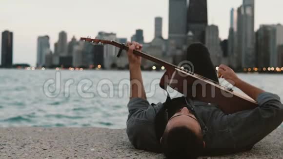 年轻时尚的男人躺在美国芝加哥的密歇根湖畔弹着吉他视频的预览图
