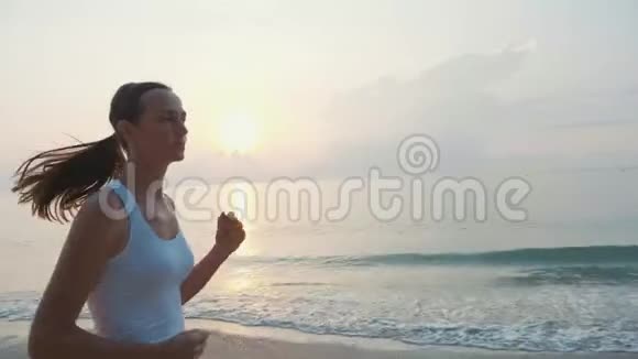 日出时在海滩上慢跑的年轻有魅力的女子视频的预览图
