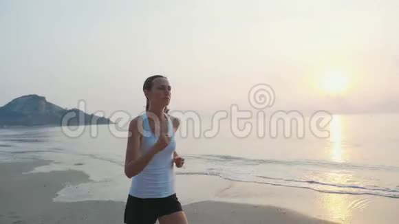 日出时在海滩上慢跑的年轻有魅力的女子视频的预览图