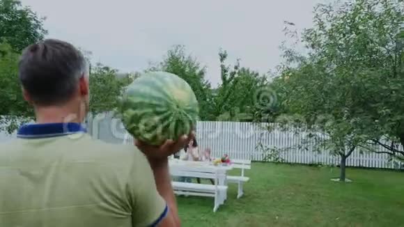 夏天在花园里爸爸背着一个大西瓜正要给家人治病和家人一起吃午饭家庭视频的预览图
