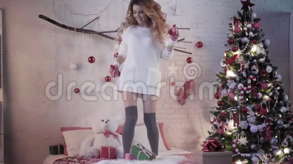 漂亮的黑发女郎穿着红手套在圣诞树附近的床上跳舞视频的预览图