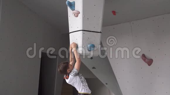 男孩爬上攀岩墙上的岩石年轻的运动员倒挂在人造岩石上慢动作视频的预览图