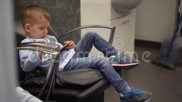 小男孩坐在椅子上玩智能手机游戏视频的预览图