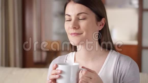 年轻女子在家里的沙发上放松漂亮的女性在客厅喝咖啡或茶视频的预览图