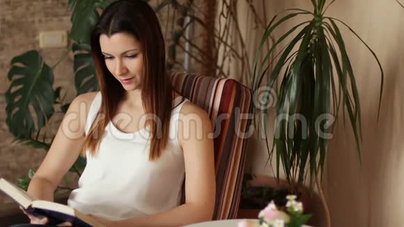 年轻漂亮的女孩坐在椅子上看书迷人的女人一边看书一边微笑积极的情绪视频的预览图