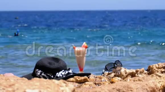 埃及海滩上的热带鲜榨果汁帽子和眼镜架在海边的岩石上视频的预览图
