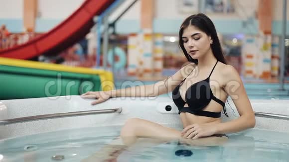戴眼镜的年轻女人在按摩浴缸里放松在相机前摆姿势漩涡浴池中女孩的肖像视频的预览图