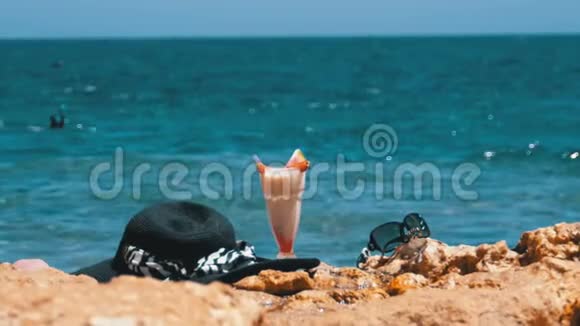 埃及海滩上的热带鲜榨果汁帽子和眼镜架在海边的岩石上视频的预览图