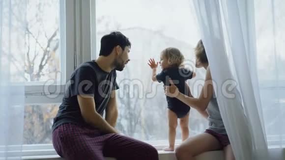 幸福的家庭年轻可爱的女儿坐在窗台上玩耍看着窗外的家视频的预览图