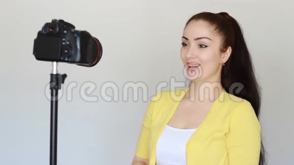快乐微笑的女性博客作者用手和说话手势在固定在三脚架上的摄像机上录制视频视频的预览图