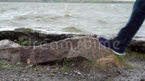 男人腿站在湖边的一块石头上洪水中的石头靠近男性的双脚通过视频的预览图