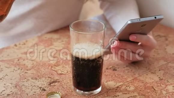 年轻漂亮的女孩在电话里读一些东西把啤酒倒进杯子里喝点东西双手特写视频的预览图