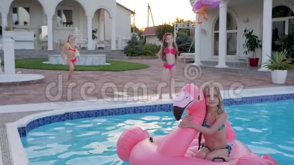 穿着泳衣跳进夏日泳池边的小女孩穿着充气火烈鸟的漂亮孩子在泳池里游泳欢快的跳跃视频的预览图