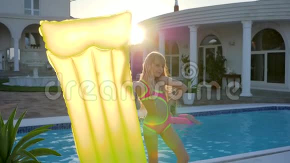 太阳落山时游泳池边手里拿着充气床垫的小女孩游泳池边穿着泳衣的可爱孩子视频的预览图