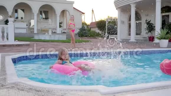 小女孩在充气戒指上游泳水溅在池边富有的小姐妹度过夏天视频的预览图
