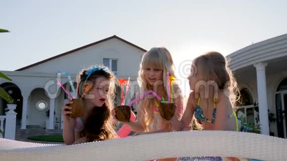 快乐的童年被宠坏的孩子在充气床垫上带着彩色鸡尾酒穿泳衣的小女孩在附近玩得很开心视频的预览图