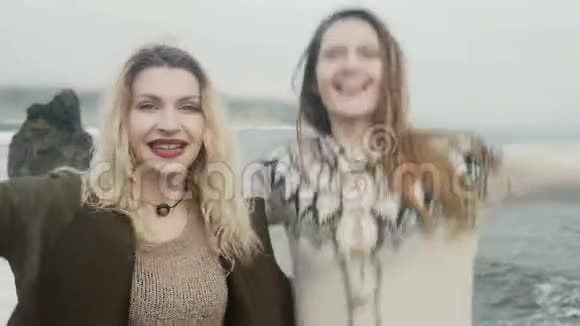 两个幸福的女人站在冰岛的黑色海滩上一起玩跳跃和微笑视频的预览图