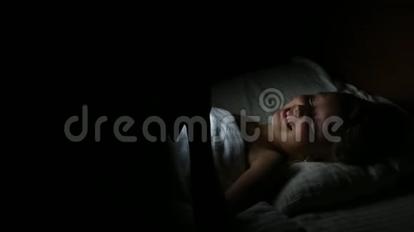 年轻的白种人女性快乐的女孩晚上躺在床上看书或玩游戏和大笑小白女孩视频的预览图