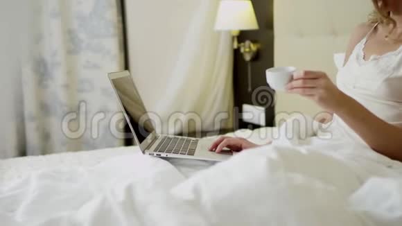 年轻女子躺在床上喝着咖啡在笔记本电脑上视频聊天视频的预览图