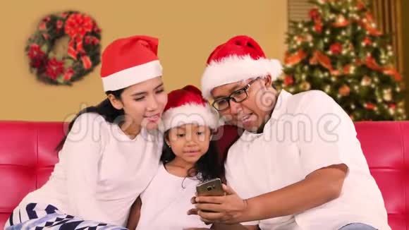 带圣诞帽的家庭在家使用智能手机视频的预览图