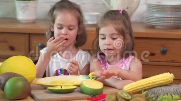 两个可爱的女孩笑着吃了一个多汁的黄色芒果视频的预览图