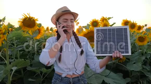 环保资源女孩用手机说话拿着太阳能电池板靠近向日葵地女人在视频的预览图
