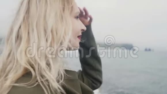 年轻的金发女人站在海滩上靠近冰岛的巨魔脚趾做着头发看着水视频的预览图