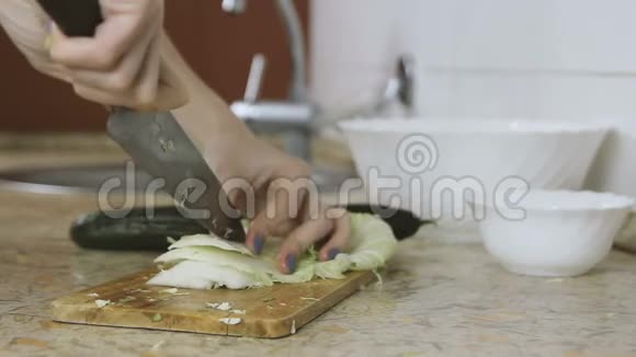 厨房餐桌上的砧板上切割大白菜的女人手的特写从侧面看视频的预览图