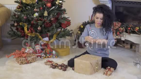 卷曲的黑发女郎在圣诞树附近包装礼物视频的预览图