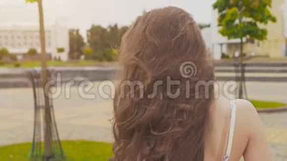 一个穿着夏装的迷人性感少女正沿着市中心的公园散步她的长发飞扬视频的预览图