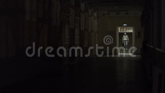 戴着帽子的悲伤男人穿着黑色的衣服走在黑暗的空荡荡的走廊上向下看孤独的内向者躲在世界上伙计视频的预览图