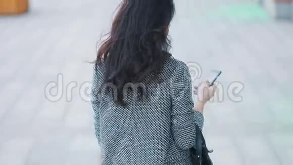 年轻漂亮的商务女孩穿着严格的灰色夹克和黑色连衣裙在城市忙碌中行走视频的预览图