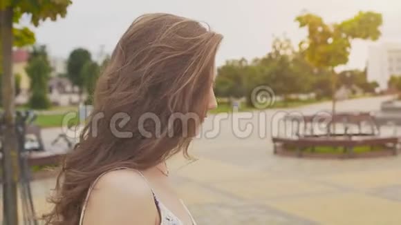 一个穿着夏装的迷人性感少女正沿着市中心的公园散步她的长发飞扬视频的预览图