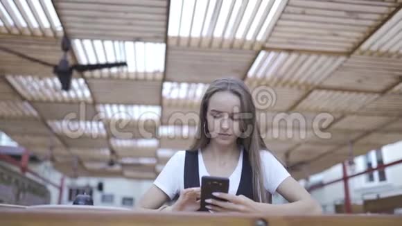 美丽的年轻女子在咖啡馆里使用现代智能手机在手机上输入短信视频的预览图