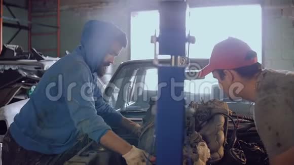 两个汽车机械师在一个微型起重机的帮助下从汽车的引擎盖上提取电机视频的预览图